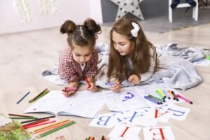 Nauka alfabetu i literek nauka alfabetu,alfabet Two-tiny-cute-girls-which-are-drawing-coloring-book-laying-floor-blanket-learning-letters